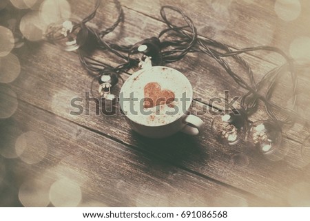 Cup of coffee and electric garland on wooden table.