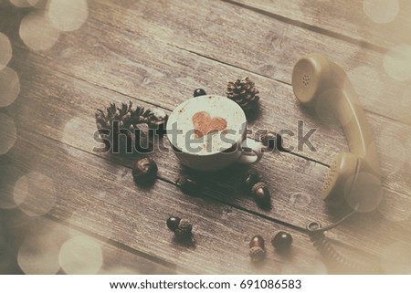 Cup of coffee with heart shape and green handset on wooden background
