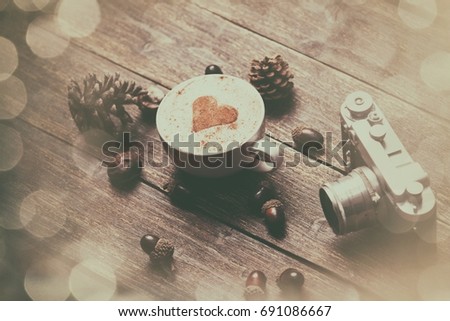 Cup of coffee with heart shape and pine cone with acorn and camera on wooden background