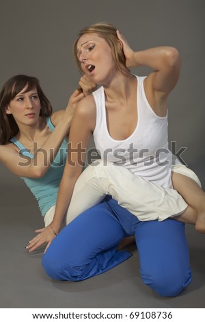two women wrestle on the ground over grey background
