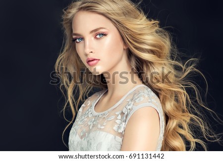 Blonde fashion  girl with long  and   shiny curly hair .  Beautiful  model  in light blue dress with wavy hairstyle .   Royalty-Free Stock Photo #691131442