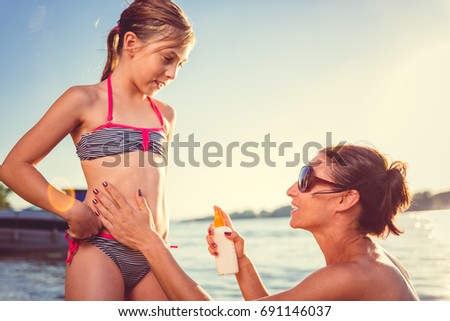 Mother applying sun protection cream to her daughter on the beach