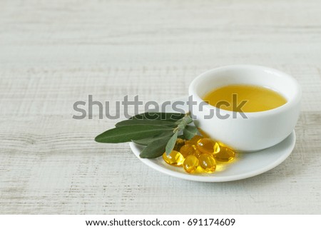 Close-up of bowl with olive oil, natural pills and olive branch kept on wooden table