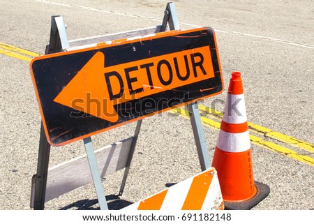 Worn Black and Orange Detour Sign next to a Orange and White Safety Cone