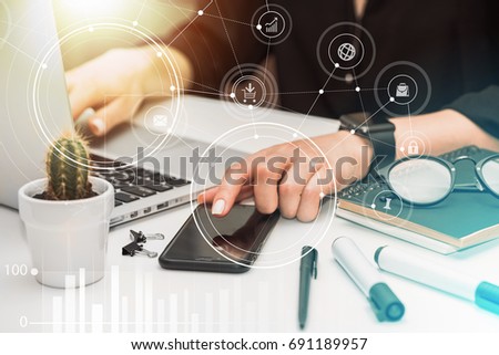 Close up of woman hands using mobile devices. Young female office manager sitting at the white desk, working on her laptop and touching screen of her mobile phone. 