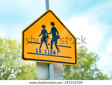 School crossing sign against blue sky with lettering cautioning drivers to go slow Royalty-Free Stock Photo #691212709