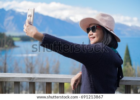 Upper body portrait of an Asian woman wearing sunglasses doing selfie with beautiful blue lake and sky in the background