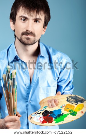 Portrait of an artist holding his brushes and paints. Shot in a studio.
