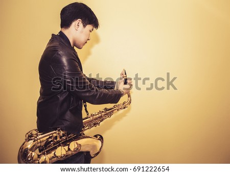 handsome young saxophone player is adjusting saxophone  reed and ligature before playing  saxophone over yellow wall background with copy space for your text
