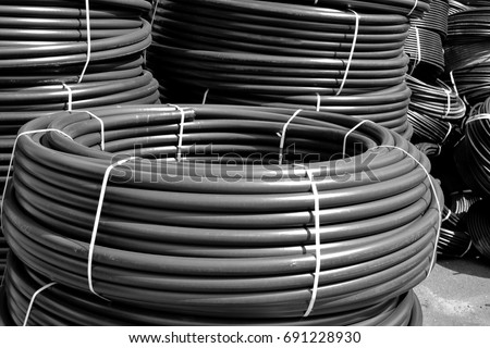Coiled black plastic pipes stored outdoors Royalty-Free Stock Photo #691228930