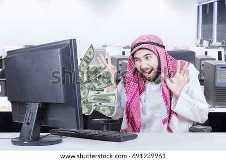 Picture of a cheerful arabian businessman looking money out of his computer
