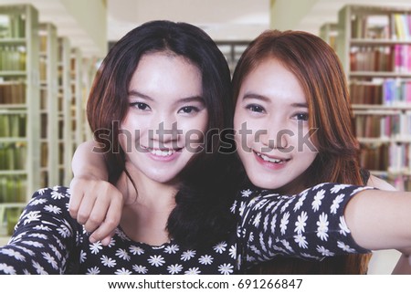 Image of two beautiful female students is taking a picture together while smiling at the library