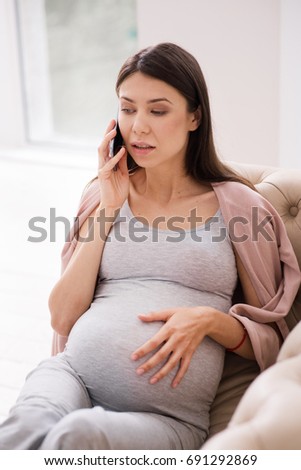 Serious pregnant female talking per telephone