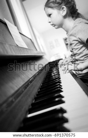 Black and white photo of a girl playing a piano, reading notes, focus on piano keys

