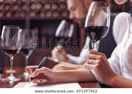 Two sommeliers, male and female tasting red wine and making notes at degustation card Royalty-Free Stock Photo #691397962