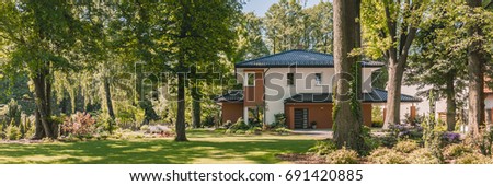 Big stylish house and enormous backyard with trees and flowers