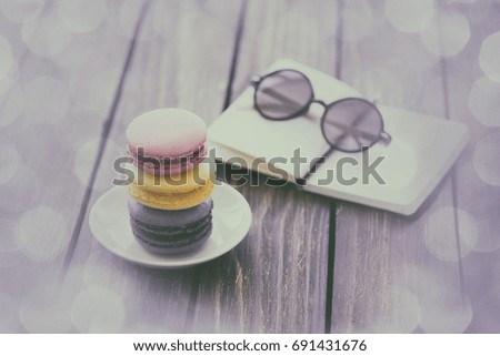 Macarons and little notebook with glasses on wooden table.