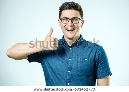 Young caucasian man with glasses showing thumbs up gesture over gray background