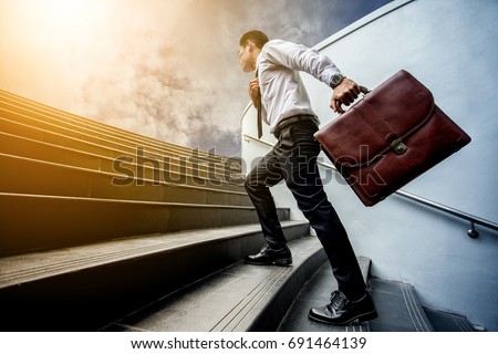 Businessman leap up the stairs to the light.He is boldly and active.. his hand hold a brown leather briefcase. Royalty-Free Stock Photo #691464139
