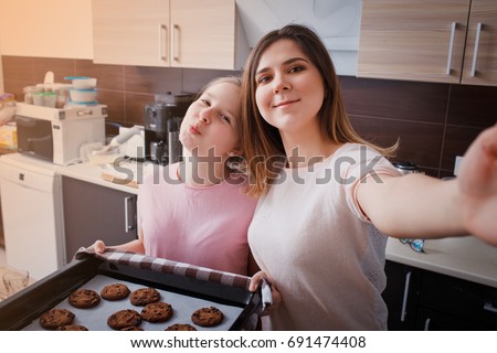 Mom and her daughter bake cookies at home in the modern kitchen and making selfie