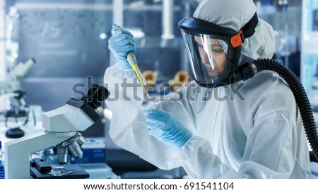 Medical Virology Research Scientist Works in a Hazmat Suit with Mask, She Uses Micropipette. She Works in a Sterile High Tech Laboratory, Research Facility. Royalty-Free Stock Photo #691541104