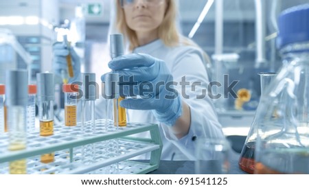 Medical Virology Research Scientist Works in a Hazmat Suit with Mask, Inspects Test Tube with Isolated Virus String from Refrigerator Box. She Works in a Sterile High Tech Laboratory Facility. Royalty-Free Stock Photo #691541125