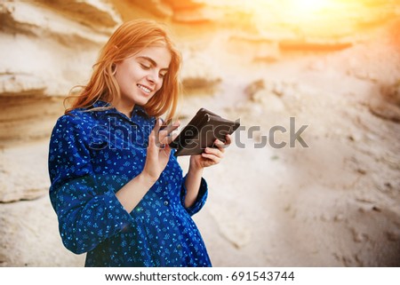 Beautiful woman smiling and looking at the screen of a tablet on the background of a sand quarry.