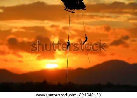 soldier silhouette in rappelling climb down from helicopter on sunset