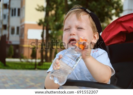 Little boy sitting in a pram and holding a drinking water bottle and capricious (crying)