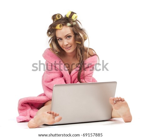 Young adult girl in pink dressing gown and with hair rollers sitting with laptop