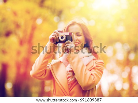 season, photography and people concept - beautiful happy young woman taking picture with vintage camera in autumn park