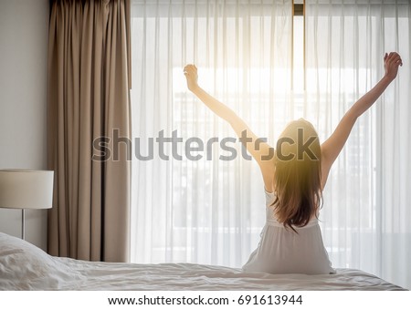 Asian woman wake up in the morning, sitting on white bed and stretching, feeling happy and fresh Royalty-Free Stock Photo #691613944