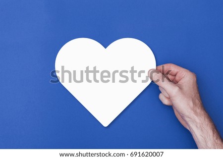 male hand holding a heart icon symbol against a blue background