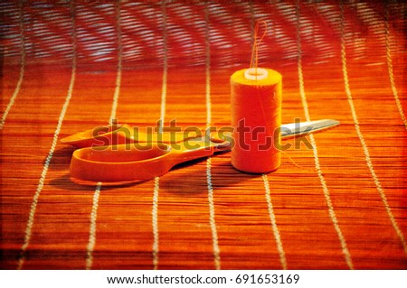 Orange scissors and thread with needle against orange background.  Horizontal photo with digital texture layer.  Copy space in lower part of image.