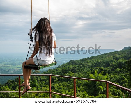 Lonely woman sit on handmade swing on the tree at top of mountain with land background, lonely and waiting for something
