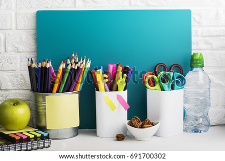 School background: a white brick wall with accessories, pencils, tetrads, scissors, an apple, pecans, a board for a substitute placed in front of her on the table. Selective focus