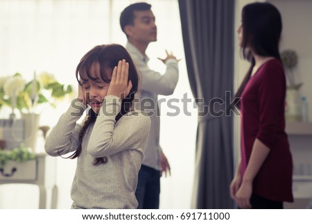 Little Girl Unhappy And Crying Fighting Parents Behind. Violence and Divorce  Family concept. Royalty-Free Stock Photo #691711000