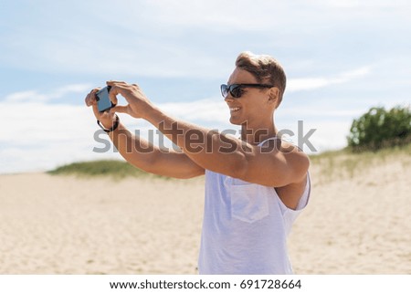 summer holidays and people concept - happy smiling young man with smartphone on beach photographing