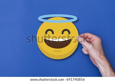 Male hand holding a emoji emoticon angel smiley head icon