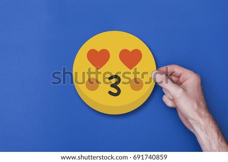 Male hand holding a emoji emoticon kissing smiley head icon