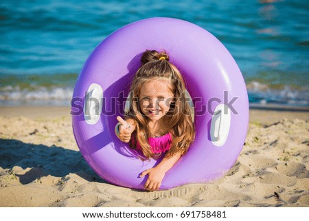 Little beautiful girl peeking out of an inflatable circle on the beach against the sea