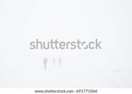Figures walk though snow and whiteout