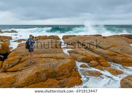 Nature travel photographer woman taking pictures on a cliff in Redbill, famous beach for wind, waves and suf. Tasmania, Australia.