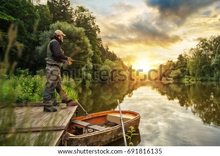 Sport fisherman hunting predator fish from wooden pier. Outdoor fishing in river during sunrise. Hunting and hobby sport.
