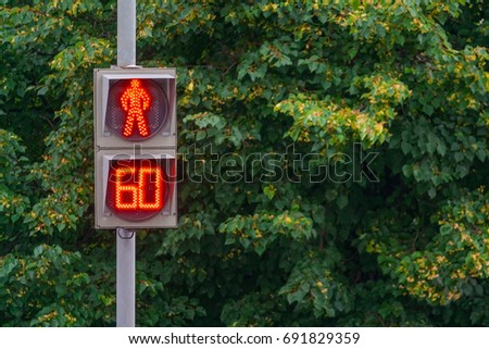 Pedestrian traffic light glowing red, counting out last minute, a background of green trees (sign, closeup)