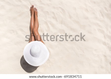 Summer holiday fashion concept - tanning woman wearing sun hat at the beach on a white sand shot from above Royalty-Free Stock Photo #691834711