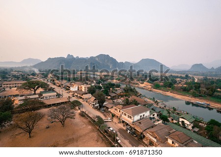 Wide angle picture of Nam Song River with tropical vegetation and houses in Vang Vieng from the top, inside the balloon in Laos, during sunrise time.