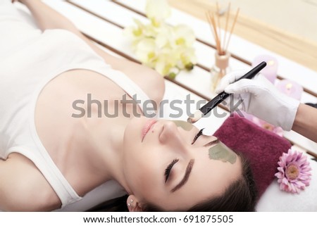 People, beauty, spa, cosmetology and skincare concept - close up of beautiful young woman lying with closed eyes and cosmetologist applying facial mask by brush in spa