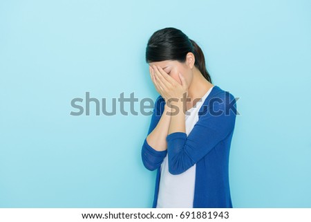 sadness young girl standing in blue background crying and using hands cover face.