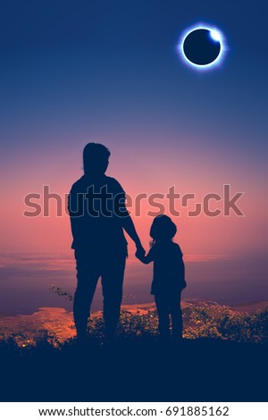 Amazing scientific natural phenomenon. Silhouette back view of Mother and daughter looking at total solar eclipse with diamond ring effect glowing on colorful sky at mountaintop. Happy family.